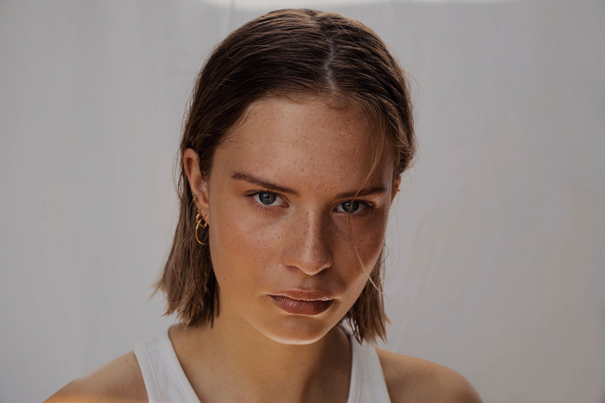 woman with radiant skin looking at the camera wearing a white tank top in front of a white background