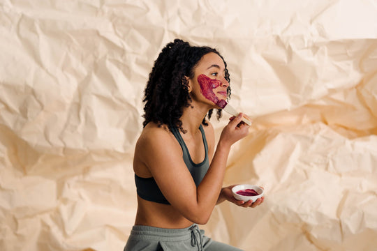 Woman applying a rose facemask using a brush and with a crinkled cream paper background