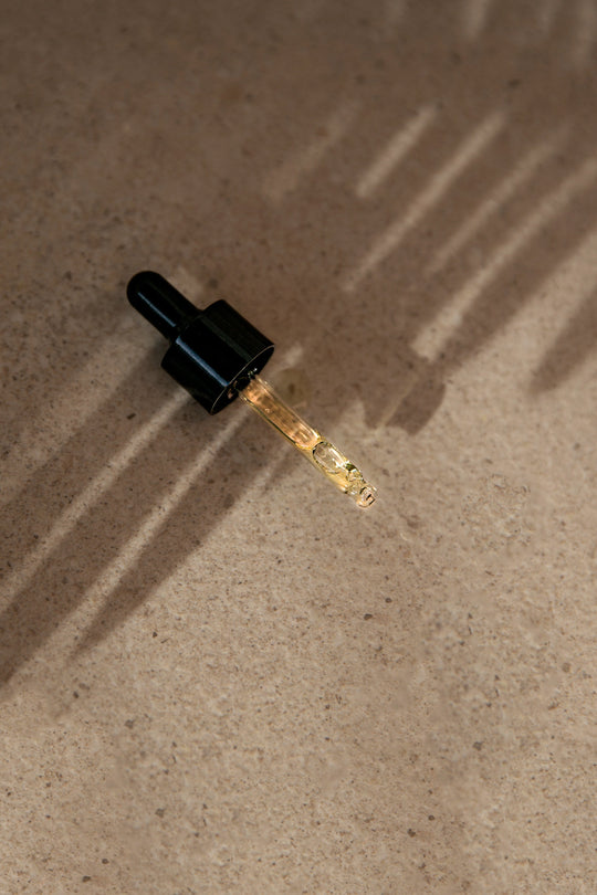 Sand colored background with shadows and a black glass dropper filled with oil