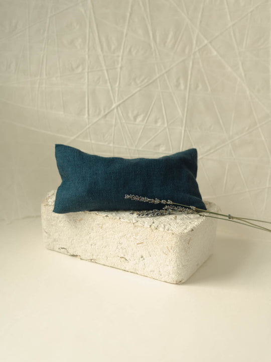 Dark blue eye pillow sitting on a white block with sprigs of lavender on the right side