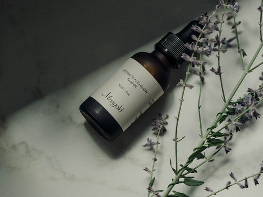 Hydrate and Glow Facial Oil by Merigold, laying on a table with lavender