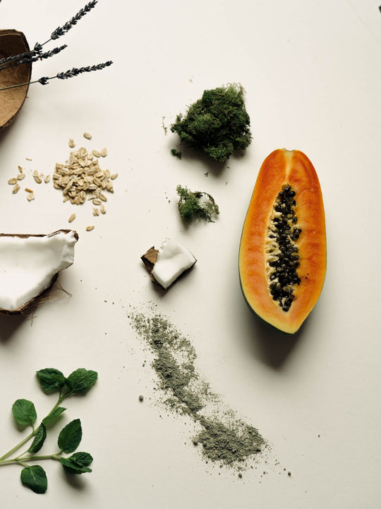 Green mask powder on white background with raw ingredients of papaya, spirulina, oat, coconut, mint 