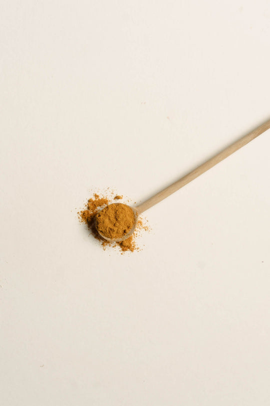 Small wooden spoon with turmeric powder, on white background