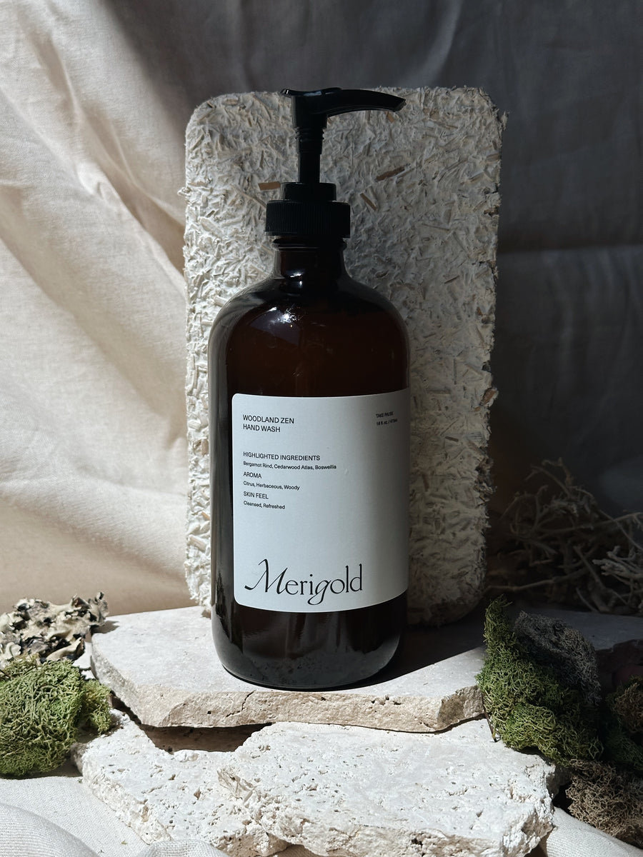 Merigold Woodland Zen Hand Soap in amber pump bottle with stylized stones, moss, and shadowed backdrop, natural aromatic hand wash.
