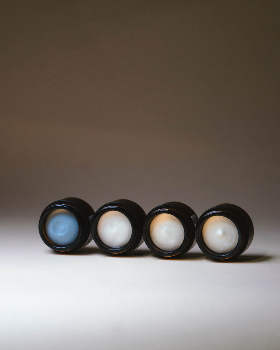 Merigold mini hand cream set with Serene Blue, Mindful Citrus, Woodland Zen, and Lavender Eucalyptus displayed in open amber jars. Showing creamy texture on a minimal background.