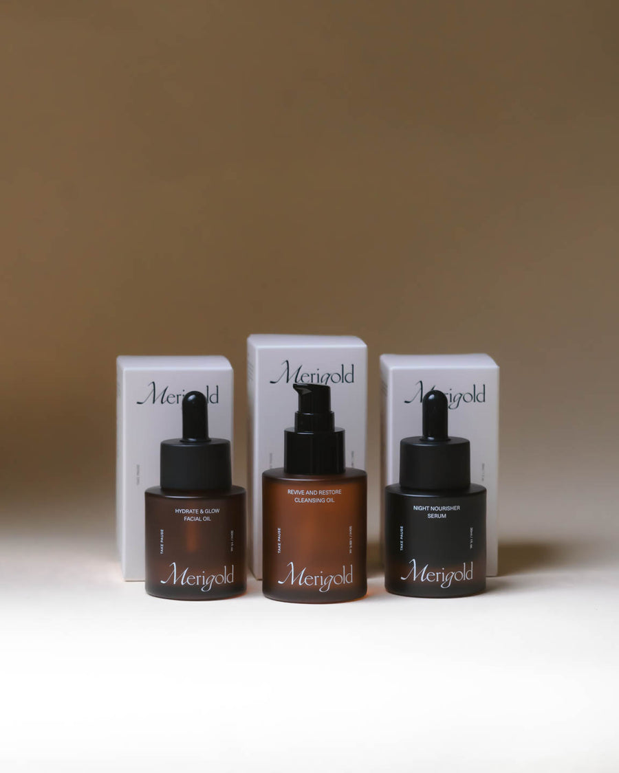Merigold Oil Trio displayed with each amber glass bottle standing in front of its coordinating white box—Revive and Restore Cleansing Oil, Hydrate and Glow Facial Oil, and Night Nourisher Serum.