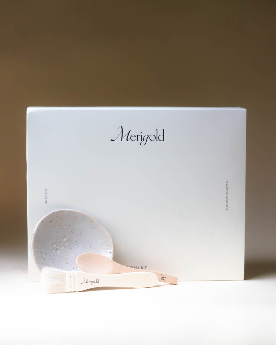 Merigold Ritual Kit with mask brush, wooden spoon, and ceramic bowl arranged in front of the white box, holistic masking ritual tools.