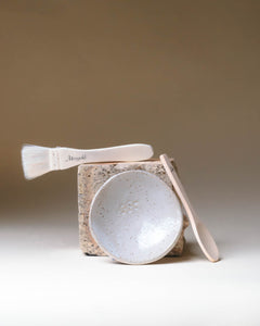 Merigold masking ritual tools—ceramic bowl, wooden spoon, and mask brush—styled on natural stone for clean skincare rituals.