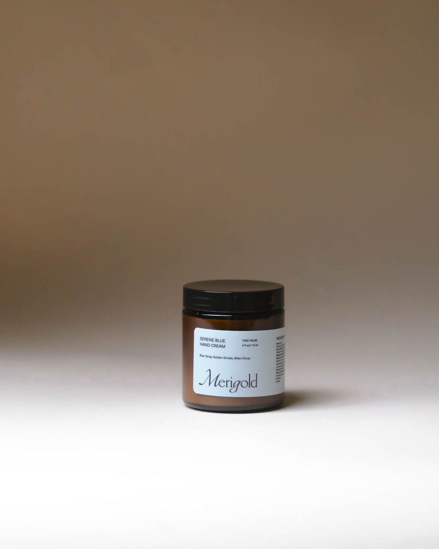Merigold Serene Blue Hand Cream with Blue Tansy in amber jar on minimal neutral backdrop.