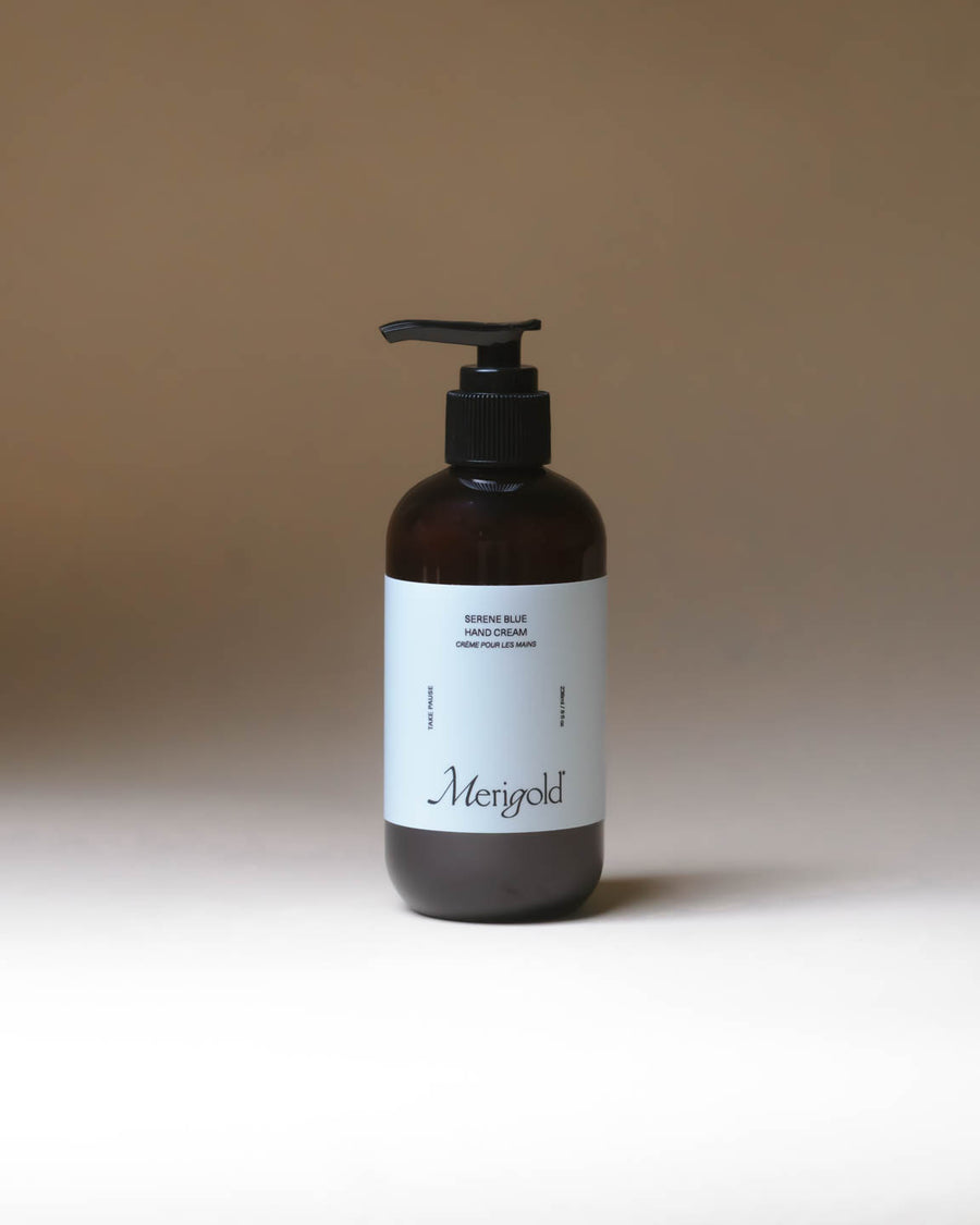 Merigold Serene Blue Hand Cream with Blue Tansy in amber pump bottle for hydrating skincare. Light blue sticker on amber bottle with minimal background. 